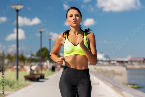fitness, sport and healthy lifestyle concept - young woman running at seaside