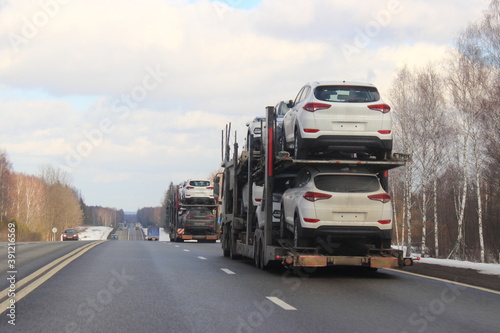 Loaded two level SUV car carrier trucks with car transporter semi trailers drive on suburban highway road at winter day, rear side view close up, delivery autos logistics, automobile transportation