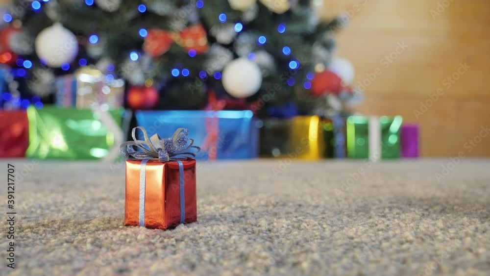 Christmas present in the red box on the carpet. Decorated Christmas tree and presents around on background. Seamlessly loop footage.