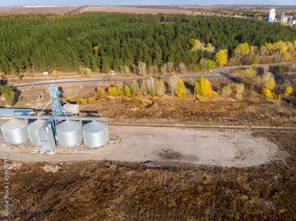 Aerial drone view modern steel agricultural grain granary silos cereal storage warehouse loading cargo grain carrier sunset. Agribuisness farmland rural industry landscape scene. Mill store facility Aerial drone view modern steel agricultural grain granary silos cereal storage warehouse loading cargo grain carrier sunset. Agribuisness farmland rural industry landscape scene. Mill store facility