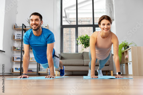 sport, fitness, lifestyle and people concept - smiling man and woman exercising and doing plank at home