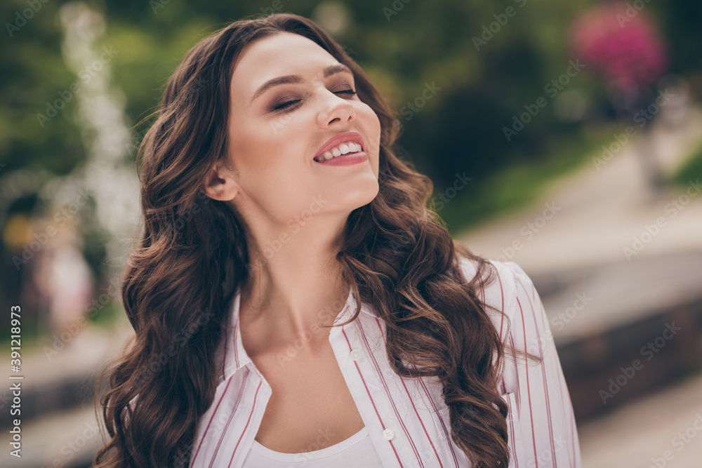 Photo portrait of nice girl with curly hair smiling enjoying fresh wind in green city park wearing striped white shirt