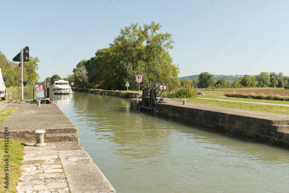 Fototapeta premium Ce bateau de plaisancier approche d'une écluse, élément indispensable sur le Canal Latéral à la Garonne pour pouvoir naviguer en toute sérénité