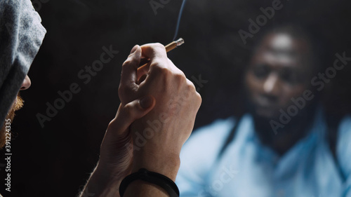 Smoking suspect with handcuffs being interviewed in interrogation room by police officer