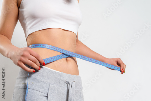 A young woman measures her waist with a measuring tape.