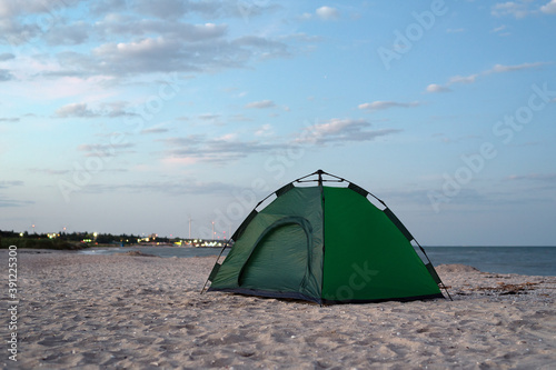 Green tent on the sandy shore against blue sky and sea background. Camping  active tourism
