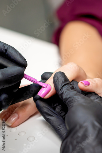 Manicure master applying pink nail polish to female nail in nail salon