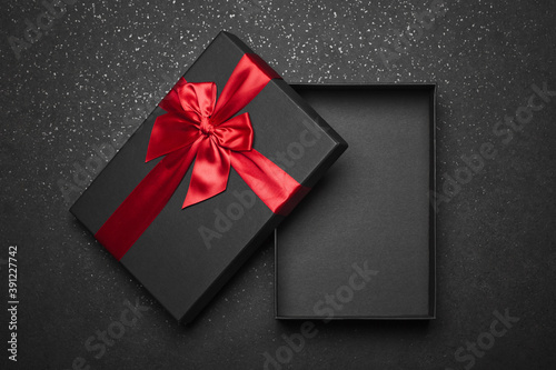 Opened black gift box with a red ribbon and a large bow on a dark granite surface. Empty box. Mockup.