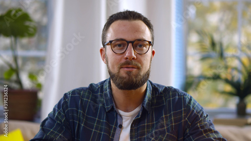 Portrait of handsome bearded man looking at speaking at camera having video call from home