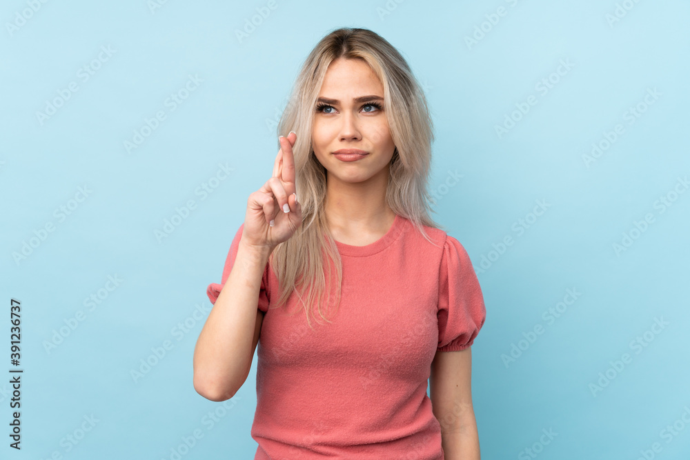 Teenager girl over isolated blue background with fingers crossing and wishing the best