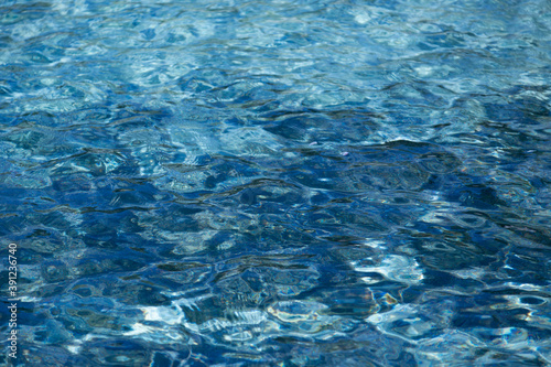 Light and dark blue water in a pool with slightly moving waves and reflections of the sun