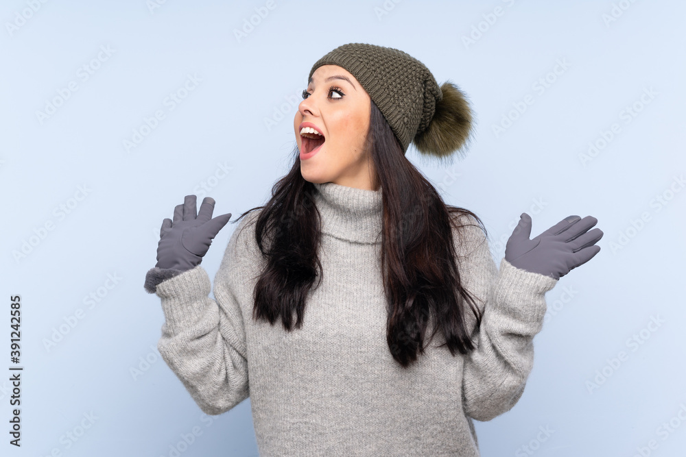 Young Colombian girl with winter hat over isolated blue background with surprise facial expression Young Colombian girl with winter hat over isolated blue background with surprise facial expression