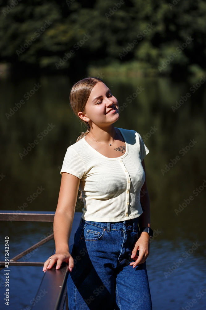 A beautiful girl of European appearance. A young woman is walking by the river. Dressed in jeans and a T-shirt.