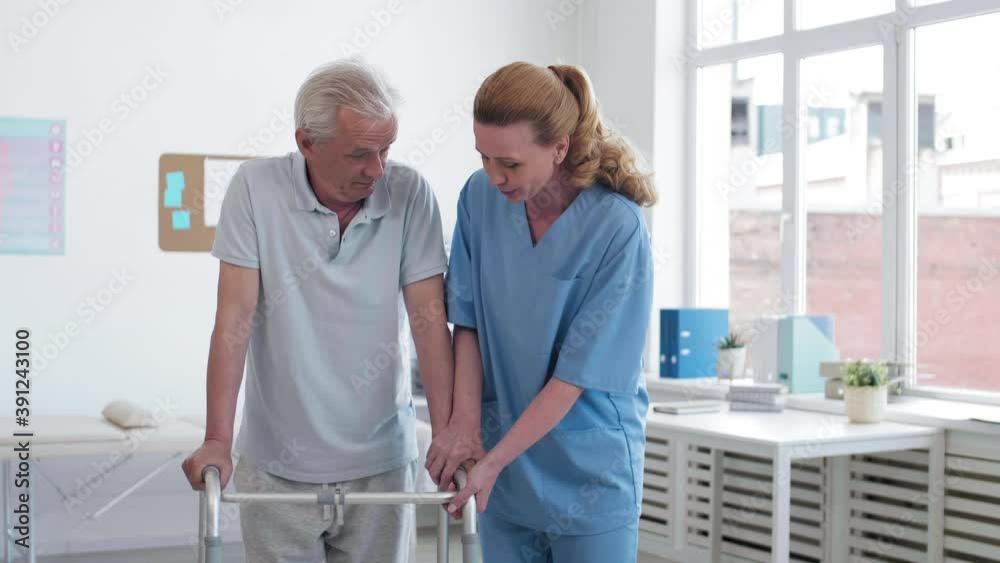 Medium shot of senior male patient walking on stilts with the help of attractive female physiotherapist in hospital. Then they looking at camera Medium shot of senior male patient walking on stilts with the help of attractive female physiotherapist in hospital. Then they looking at camera
