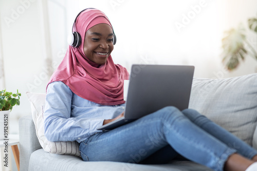 Home Pastime. Black Muslim Woman In Hijab Relaxing With Laptop And Coffee