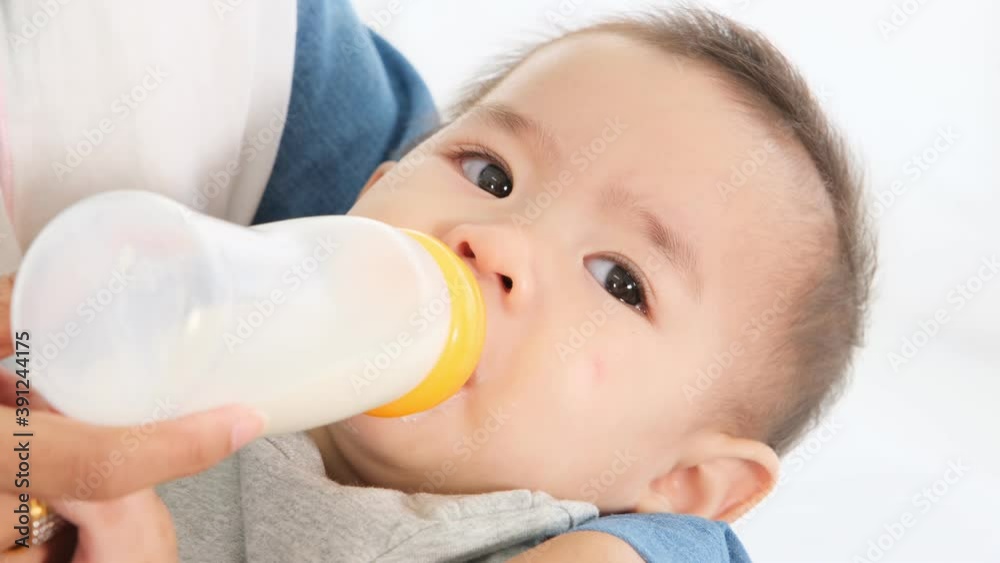 Asian young mother holding newborn baby girl in arms and feeding cute infant from milk bottle on bed. Asian young mother holding newborn baby girl in arms and feeding cute infant from milk bottle on bed.