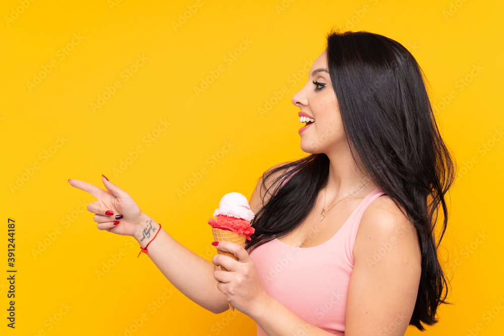 Young Colombian girl holding an cornet ice cream over isolated yellow background pointing to the side to present a product Young Colombian girl holding an cornet ice cream over isolated yellow background pointing to the side to present a product