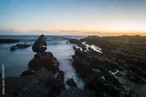 fotógrafo agachado sobre una roca tomando una fotografía del atardecer