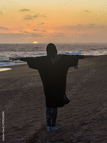 silueta de una persona con los brazos levantados con el mar y el sol de fondo al atardecer