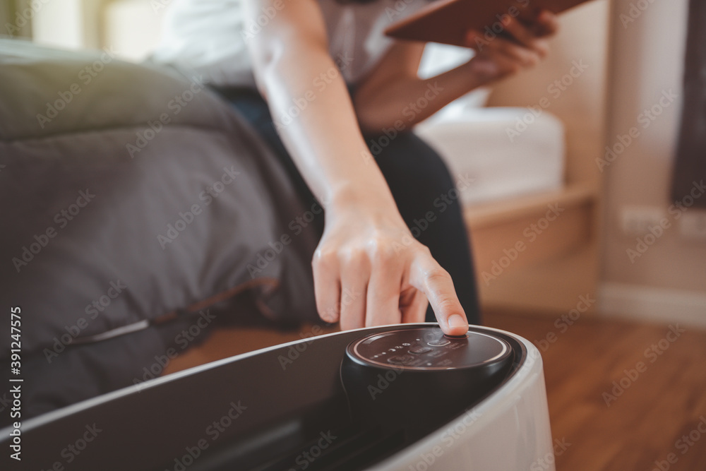 Fototapeta premium Asian sleepy woman trying to press a button on the portable air purifier machine in a bedroom.