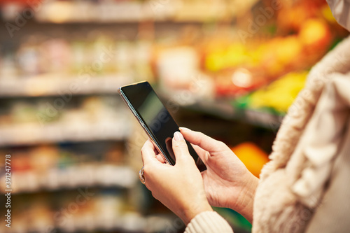 Adult woman in medical mask using smartphone and shopping for groceries