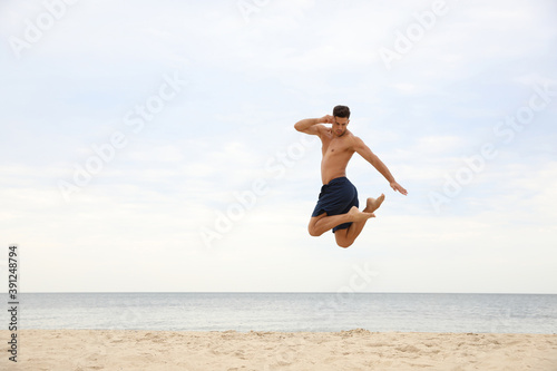 Muscular man jumping on beach, space for text. Body training