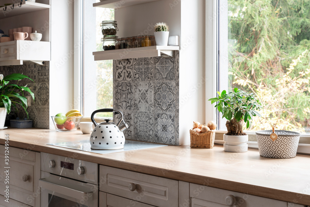 Φωτογραφία Cozy white kitchen with wooden furniture and counter with design tiles and window with plant