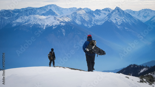 Two adventurers in front of snow-capped mountain ranges in BC, Canada, bathed in blue light (early winter).