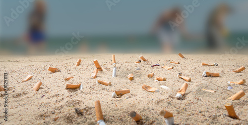 cigarette butts pollute a beach where unrecognizable people go on vacation
