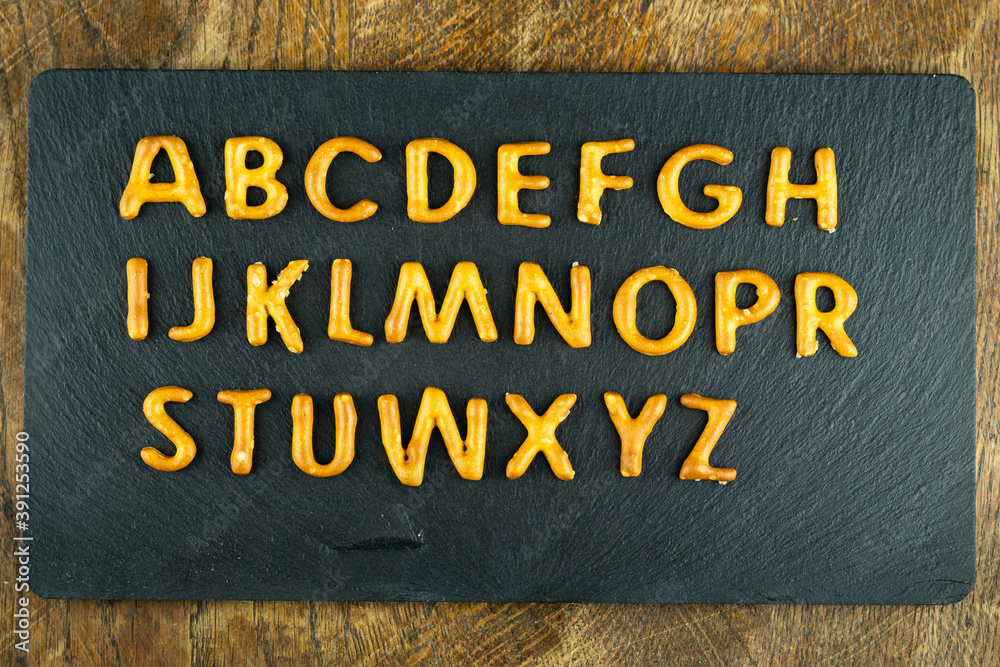 snack alphabet made of salty sticks letters on black stone at wooden background. Pretzels, salty snacks text.