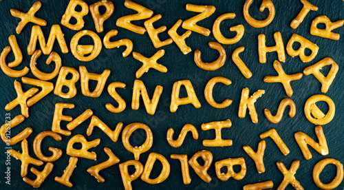 Obraz na płótnie Snack text among salty sticks letters, alphabet on black stone background. Junk food, unhealthy diet concept. w salonie
