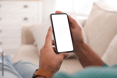 Man holding mobile phone with empty screen indoors, closeup © New Africa