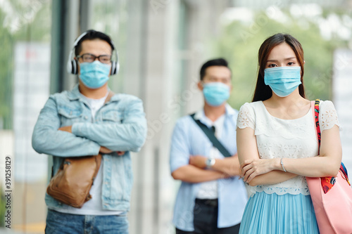 Sad serious young Asian woman standing in the street with medical mask on her face