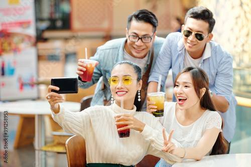 Group of excited young Vietnamese people posing for selfie with cocktails in hands