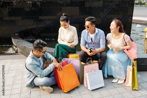 Joyful friends sitting outdoors with paper bags around after shopping in mall © DragonImages