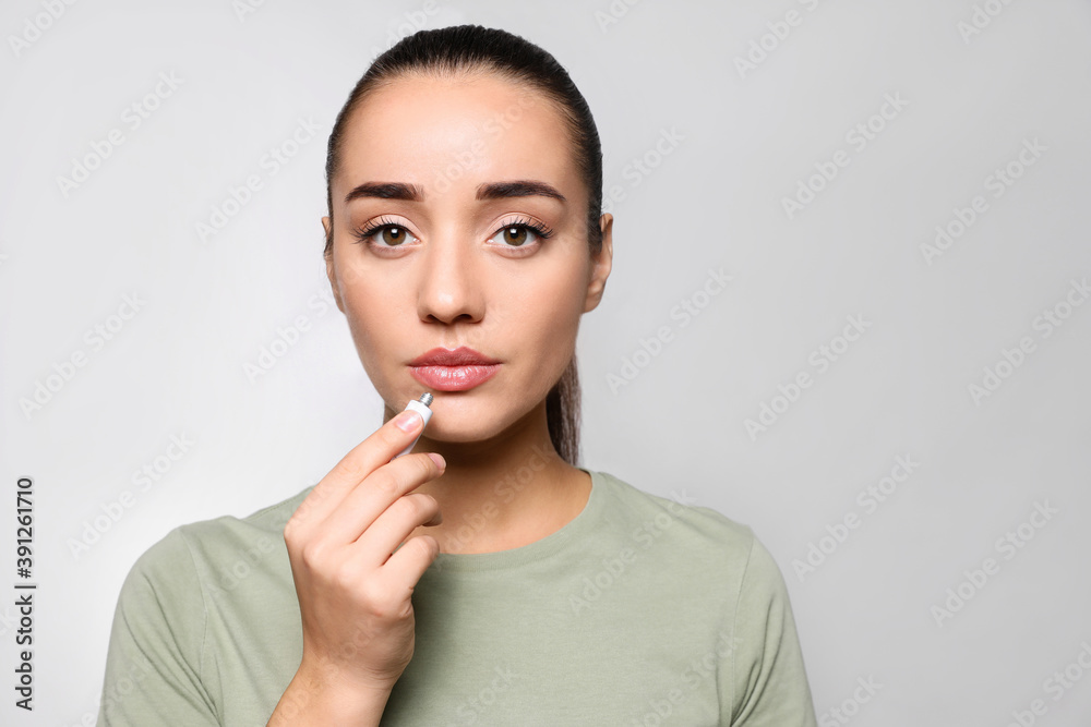 Woman with herpes applying cream on lips against light grey background. Space for text