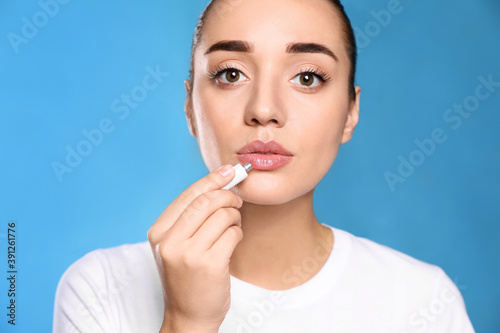 Woman with herpes applying cream on lips against light blue background