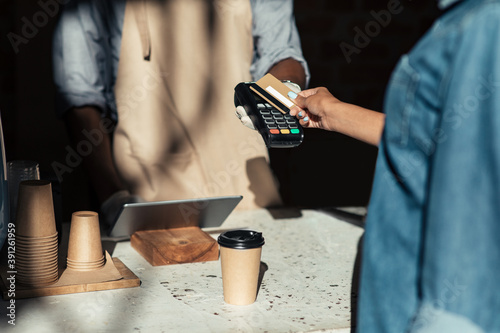 Slika na platnu Client pays to coffee bill, millennial african american bartender in apron gives