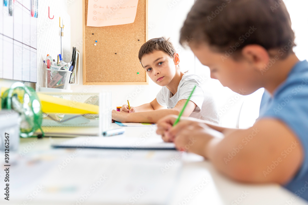Two boys studying and doing homework sitting at their desk in their bedroom at home Two boys studying and doing homework sitting at their desk in their bedroom at home