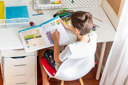 Boy studying and doing homework sitting at his desk in his bedroom at home