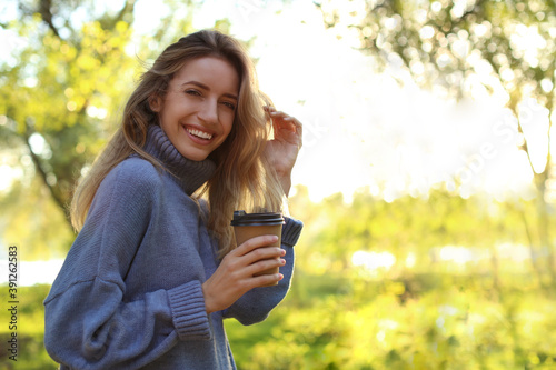 Beautiful young woman with coffee cup wearing stylish sweater in autumn park