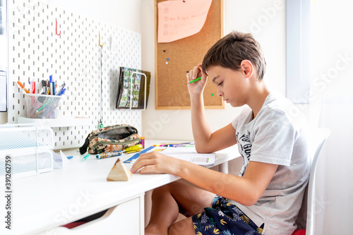 Boy studying and doing homework sitting at his desk in his bedroom at home