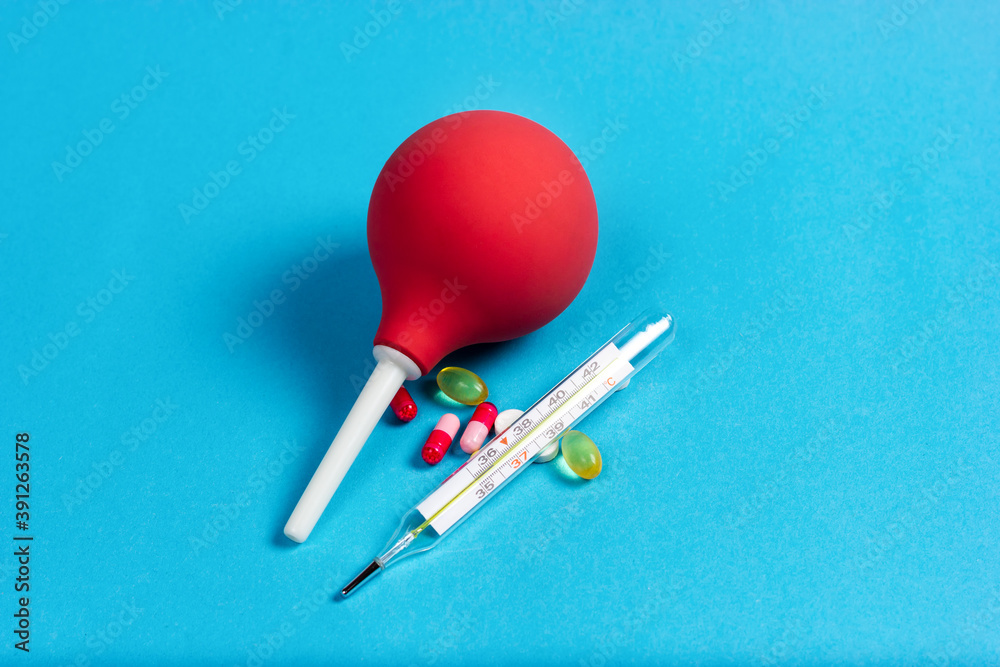 Medical pear, enema for procedures, mercury thermometer and pills on a blue background. Food poisoning. Medical pear, enema for procedures, mercury thermometer and pills on a blue background. Food poisoning.