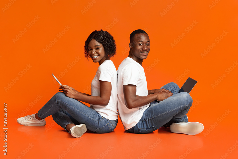 Cheerful black couple using social media over orange Cheerful black couple using social media over orange