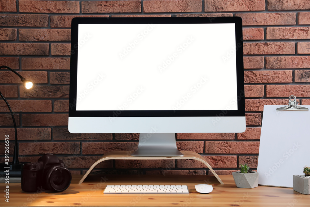 Fototapeta premium Comfortable workplace with modern computer on wooden table near brick wall. Space for text