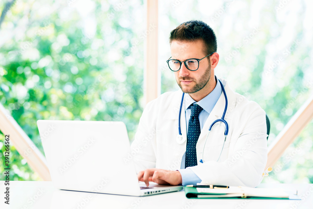 Portrait shot of male doctor working on notebook while sitting at desk in doctor's office. Portrait shot of male doctor working on notebook while sitting at desk in doctor's office.