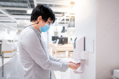 Asian man using automatic alcohol dispenser for cleaning hand in office. Infection prevention concept. Save and clean in public building.