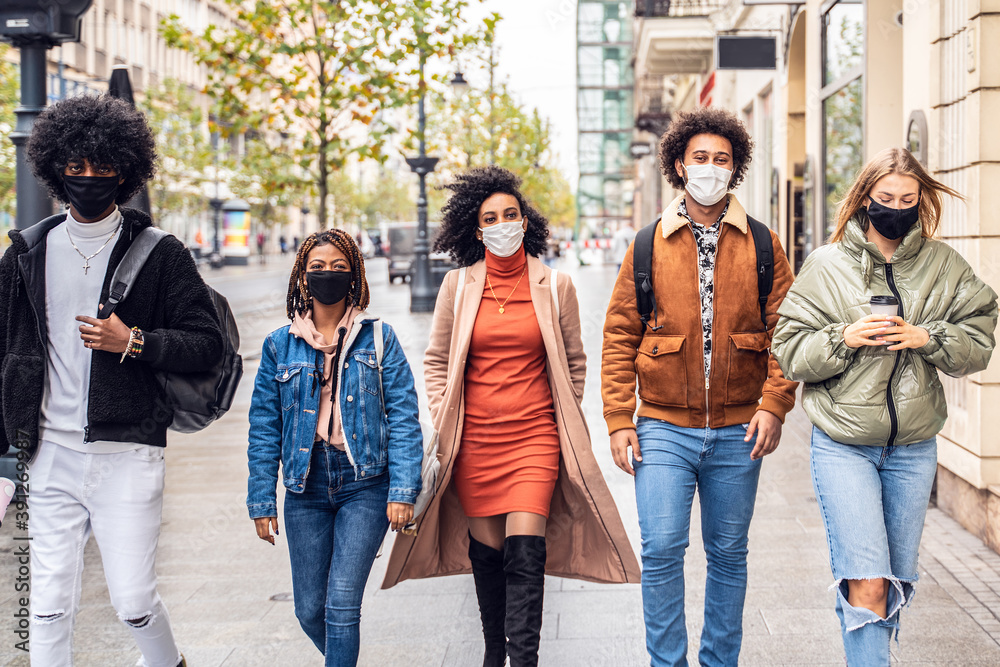Group of multiracial friends walking on city street with protective face mask.