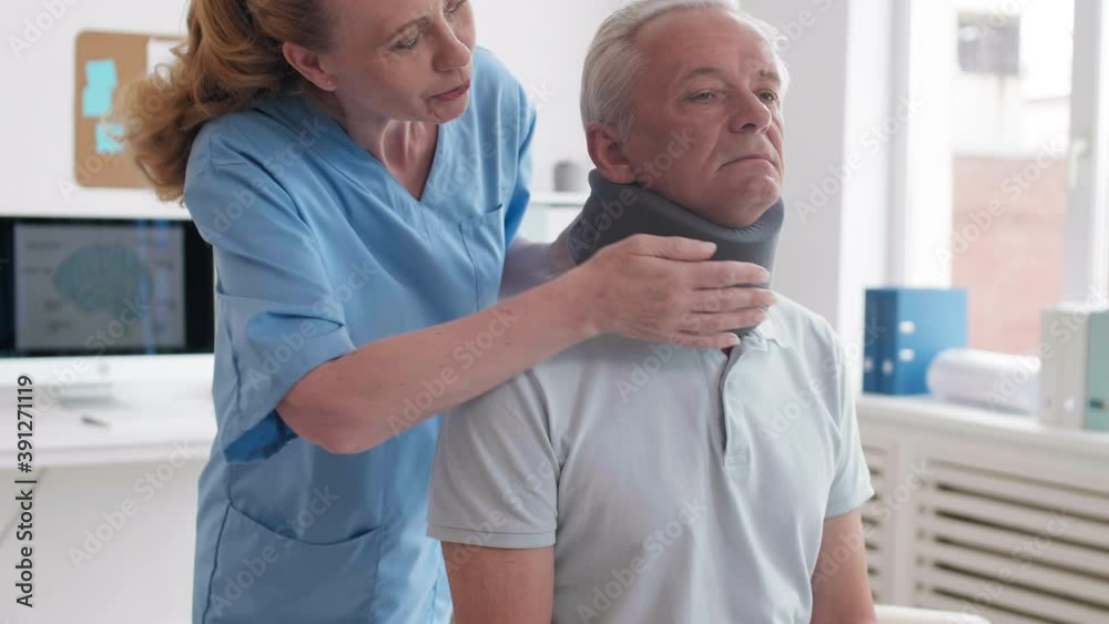 Medium shot of female physiotherapist putting bandage on neck of aged Caucasian man sitting on exam couch in medical office Medium shot of female physiotherapist putting bandage on neck of aged Caucasian man sitting on exam couch in medical office