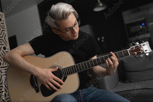 Man with white hair wearing glasses playing guitar at home